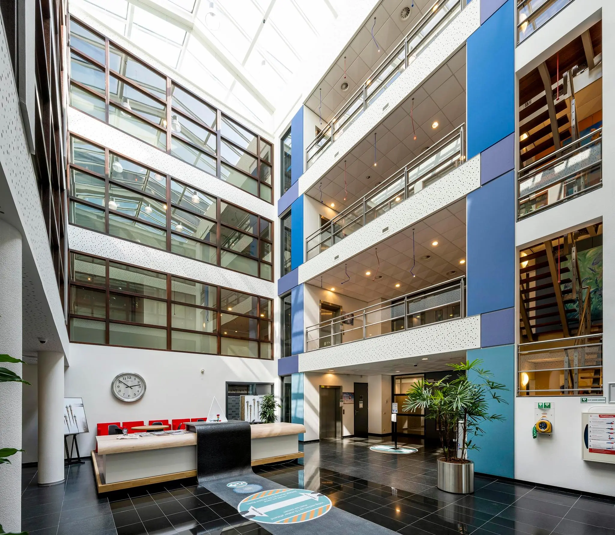 Moderne, lichte entreehal van een kantoorgebouw aan de K.P. van der Mandelelaan met balie, glazen dak en meerdere verdiepingen met galerijen.